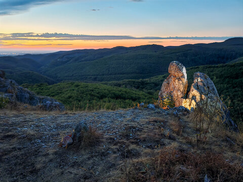 Limestone rock formations illuminated by warm early morning light above the Garadna Valley at Kopus-ko in the Bukk Mountains, Hungary, with colorful dawn sky and distant mountain ridges.