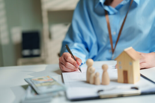 Estate planning attorney finalizing a living trust and will on a clipboard beside wooden family figurines, a model house, and cash, generational wealth transfer, inheritance, and asset protection