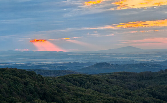 Dramatic pink rays of early morning sunlight shining through clouds above the distant Tokaj Mountain, seen from the Bukk Mountains in northern Hungary.