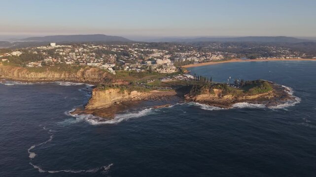 Terrigal Skillion headland and sweeping coastal bay glow at sunrise, drone tracking right establishing backdrop