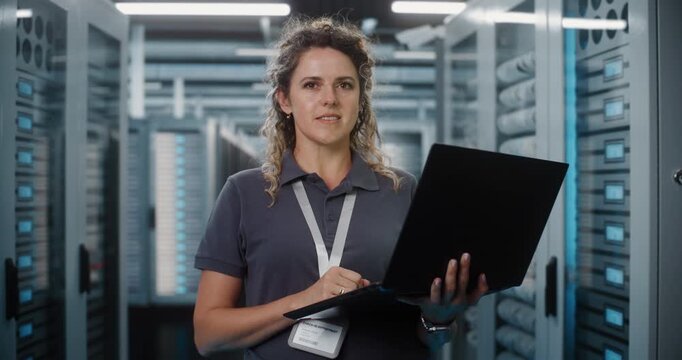 Standing in Server Room Hallway, Female IT Specialist Operates Laptop to Diagnose Cybersecurity Data and Server Rack Metrics. Advanced Cloud Management Protects Enterprise Network Databases. Portrait.
