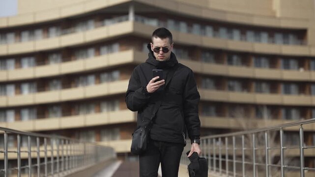 Young business freelancer man is standing outside in front of a building, looking at his cell phone. Concept of detachment and disconnection from the world around him