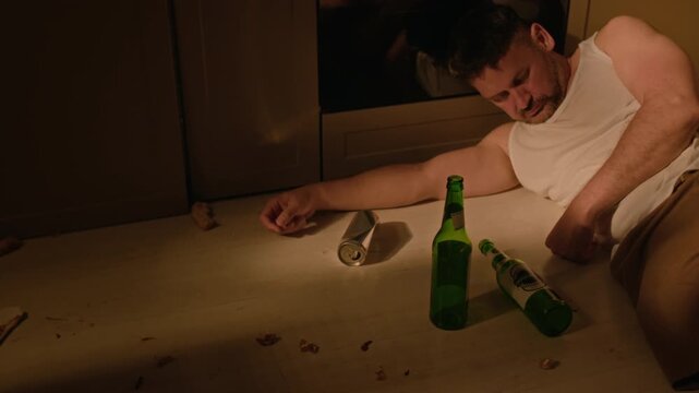 Middle aged Caucasian man suffering from hangover waking up on floor and drinking beer. Footage suitable for addiction recovery campaigns and substance abuse awareness projects