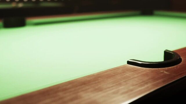 A close up of a pool table featuring a smooth green felt top and polished wooden edges shines under dim lighting. The scene invites players to enjoy a game.