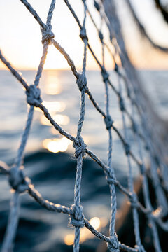 Close up of a fishing net or safety net on a boat with the ocean and sunset in the background.