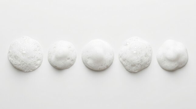 White soap foam bubbles arranged in a horizontal row on a clean studio background.
