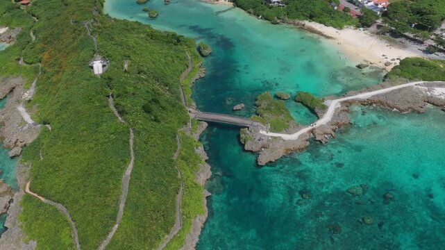 Horizontal cameo moving backwards while rising from an overhead angle, revealing the turquoise waters and rocky coastline near Shigira, Miyako, Okinawa, Japan