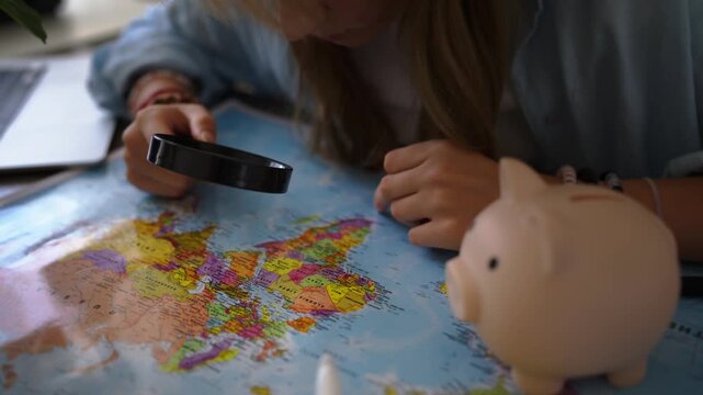 Teenager girl planning dream vacation by examining world map with a magnifying glass, with a piggy bank nearby symbolizing saving money for travel, adventure, and exploration