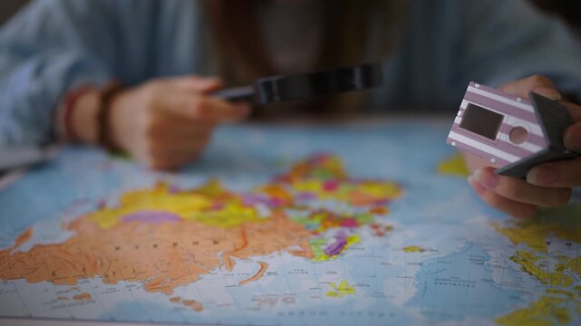 Woman with a magnifying glass meticulously studying a world map, holding a small house model, symbolizing the dream of relocating, investing, or finding a new home abroad