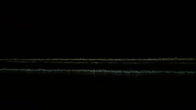 Cinematic 4K video of dramatic ocean waves crashing onto the sandy beach shoreline at night. Detailed white foam and dark atmospheric water contrast under nighttime lighting