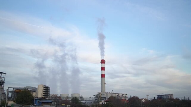 A large red and white tower with smoke coming out of it. The sky is cloudy and the sun is not visible