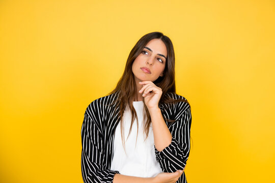 Young woman pondering a thought or idea, looking up with a pensive expression, considering future options and making a choice against a vibrant yellow background