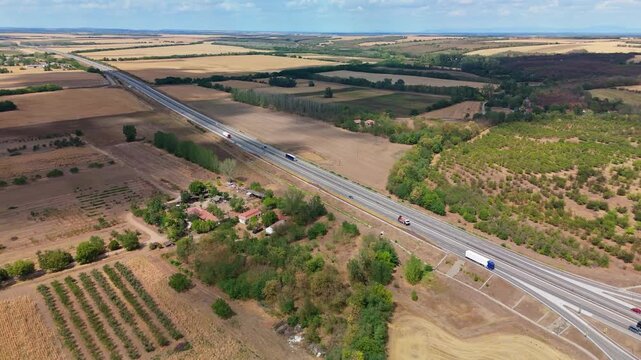 Hungary's M4 motorway near Gerje and Pilis with cars and trucks crossing rural farmland and patchwork fields beside village houses in summer, viewed by drone.