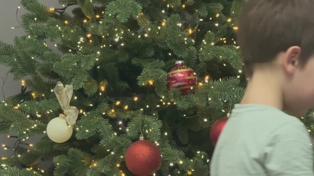 Child hanging ornament on Christmas tree. Warm festive moment and holiday preparation. 