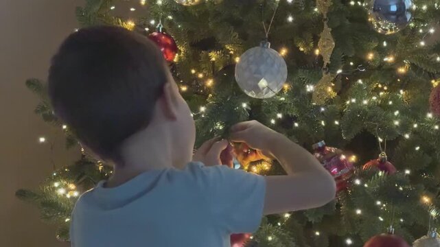 Child placing ornament on Christmas tree in close view. Focus on festive preparation and family routine.