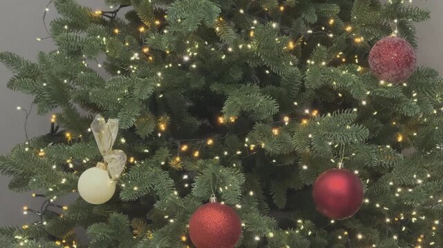 Close up of Christmas tree ornaments with red balls and glowing lights. Festive decoration detail. Perfect for holiday branding and seasonal visuals.