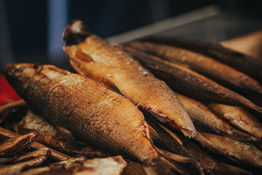 Freshly smoked fish displayed in a market setting, showcasing various sizes and textures of the fish with a blurred background of additional seafood products