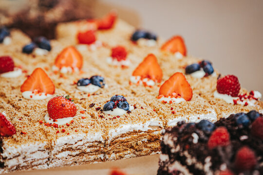 Layered dessert with cream, strawberries, blueberries, and raspberries arranged on a wooden surface, showcasing a variety of textures and colors in a close-up view