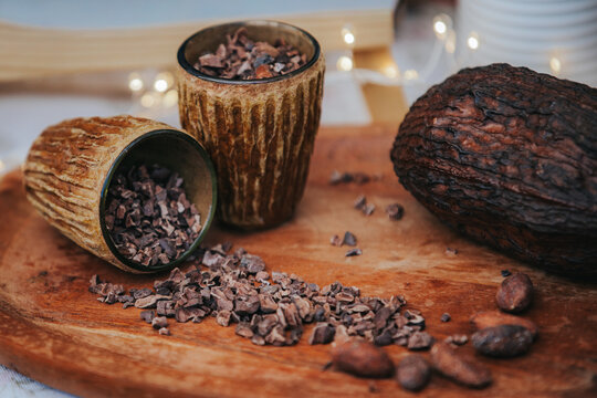 Cocoa beans and chocolate pieces in rustic bowls on wooden platter with blurred background and soft lighting creating a warm, inviting atmosphere for culinary use