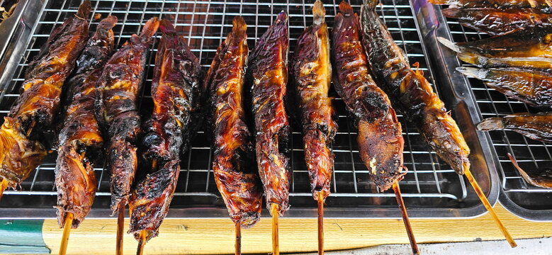 Herb-marinated catfish is skewered and grilled until cooked and fragrant. It placed on a stainless steel grill for serving. Clarias skin is slightly crispy and usually served with Jaew dipping sauce.
