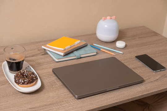 Workspace with laptop, notebooks, coffee, and snacks on a wooden table
