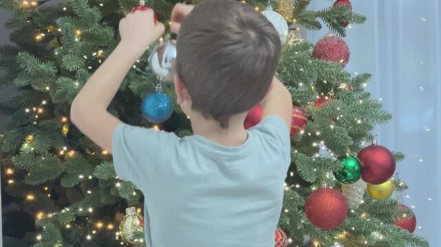 Child placing silver ornament on Christmas tree. Close up festive detail. Suitable for holiday design and seasonal branding.