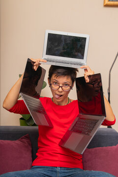 Person balancing three laptops while sitting on a couch at home and making a funny face