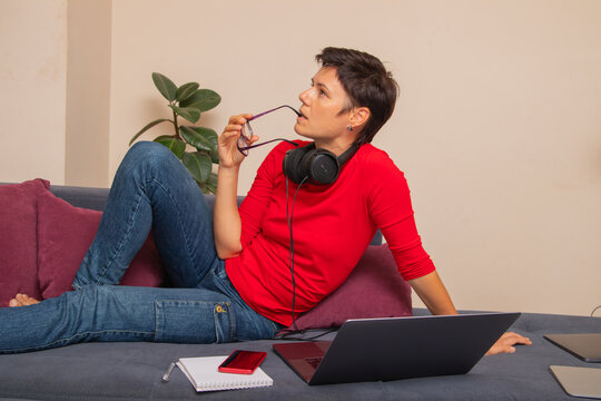 Woman sits on couch with laptop and notebook during learning session at home
