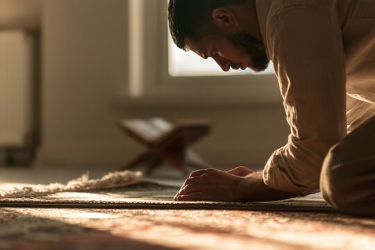 Muslim man praying on a rug with quran