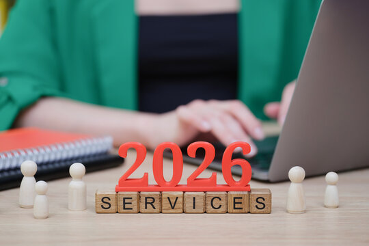 On a work desk, a laptop is open while someone types away. Colorful notes and wooden figures surround the bold 2026 and services lettering, symbolizing future planning.