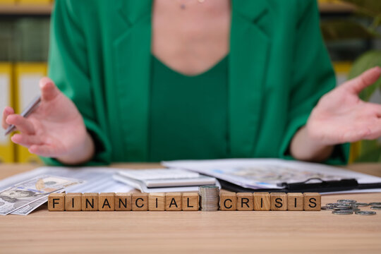 A person dressed in a green blazer sits at a table surrounded by financial documents and coins while discussing the challenges of a financial crisis.