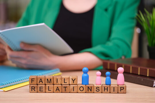 In a warm study space, a person sits comfortably with a notepad, examining wooden blocks that spell family relationship. Colorful figurines represent diverse family bonds.