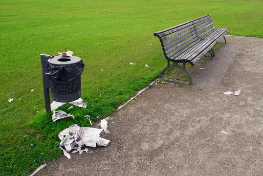 rubbish outside a garbage bin and a bench in a public park
