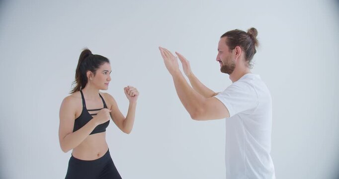 A personal trainer coaches a determined woman on boxing techniques, guiding her stance and form during a private lesson in a bright minimalist fitness studio.