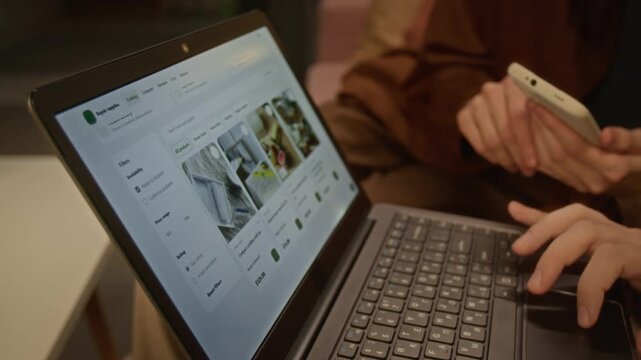 Unrecognizable couple browsing online store catalog on laptop and pointing at screen while holding smartphone. Ideal for e-commerce advertising, retail shopping apps and digital consumer campaigns