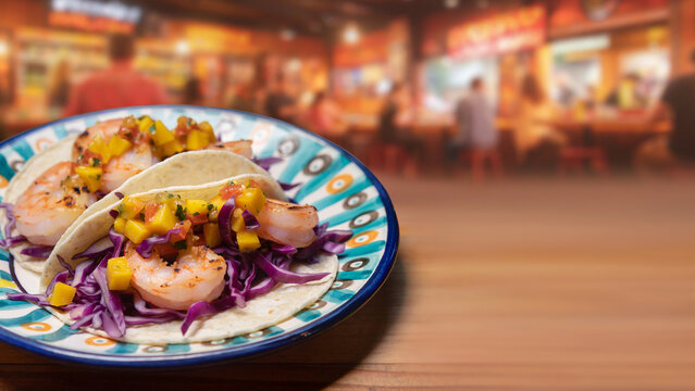 Colorful shrimp tacos with purple cabbage and mango salsa with blurred cantina background banner.