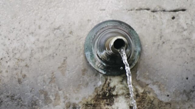 A water fountain with a spout that is dripping water. The fountain is located in a courtyard