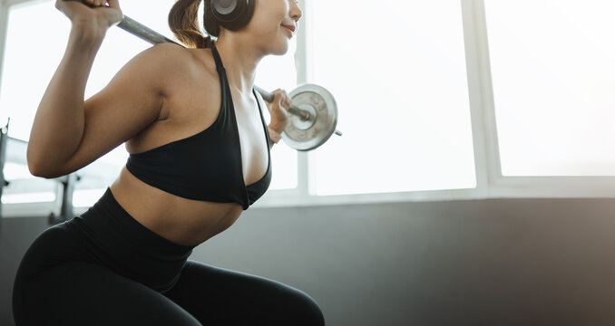 A squat under a barbell turns training into strength for the athlete by tall windows, while another squat keeps the barbell level as training builds strength for the athlete wearing large audio gear.