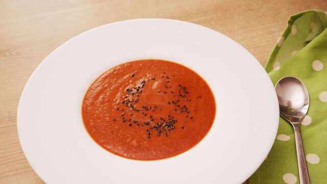 Close up shot of hand sprinkling black sesame seeds over creamy tomato and red pepper soup in white bowl. Professional food styling garnish process.