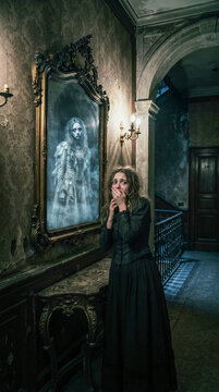 Un pasillo g&oacute;tico y l&uacute;gubre de una mansi&oacute;n abandonada, con espejos antiguos que muestran reflejos de figuras fantasmales y atormentadas. La luz de las velas crea sombras espeluznantes.