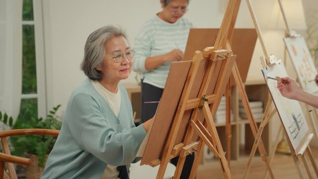 Happy senior elderly woman painting during an art therapy activity in a nursing home with caregiver support, promoting mental health, emotional wellbeing, creativity and active aging.
