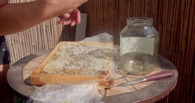 hands and upper body of adult male unwrapping and arranging loaf on wooden cutting board beside knife and glass jar on small tiled outdoor table, bamboo privacy