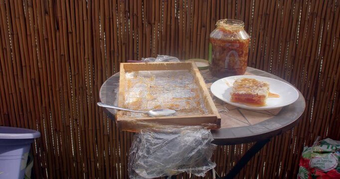 golden honeycomb on sunlit outdoor mosaic table beside glass jar, spoon, bamboo backdrop, showing sticky amber syrup and rustic serving styling for gourmet bites