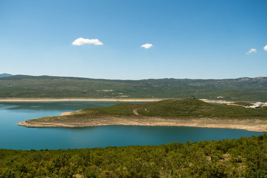 Panoramic view of a blue artificial lake surrounded by green hills.