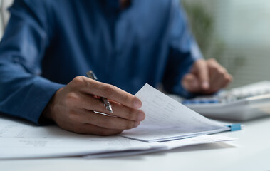 Businessman reviewing financial documents and using calculator at office desk represents...