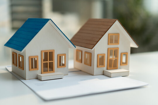 Two miniature houses on property documents represent real estate choices, home comparison, residential investment, buying decisions and selecting suitable housing for ownership or relocation.