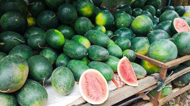 Camera approaches a large pile of fresh watermelons with sliced fruit on display