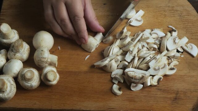 Cutting fresh mushrooms with a knife on a cutting board on a wooden table