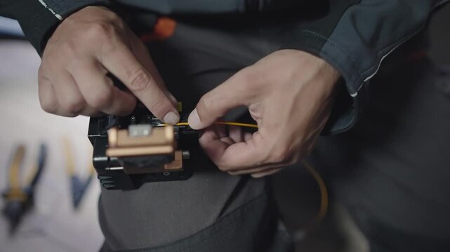 A person is holding a device with a yellow wire in their hand. The device is a fiber optic cable