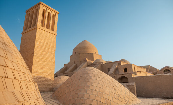 Jameh Mosque of Ardestan featuring a traditional water reservoir (Ab Anbar) dome and a prominent windcatcher (Badgir) in the foreground under a clear sky, showcasing historical Persian architecture.